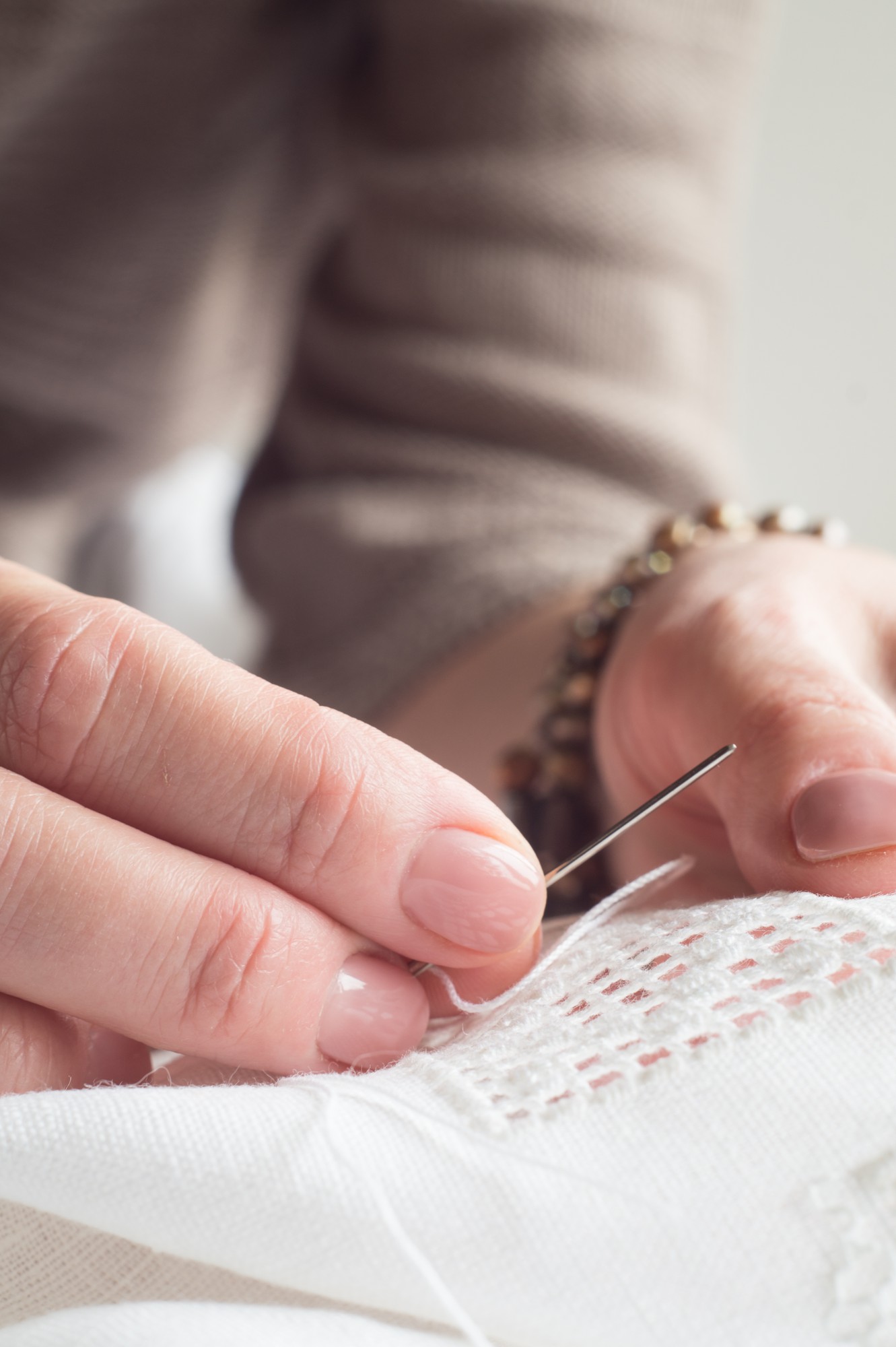 hands threading needle over linen with embroidered motif